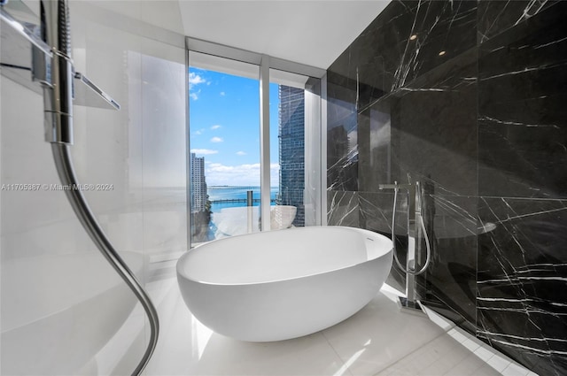 bathroom featuring tile patterned floors, a tub to relax in, a water view, and tile walls