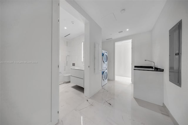 corridor featuring sink, electric panel, and stacked washer and clothes dryer