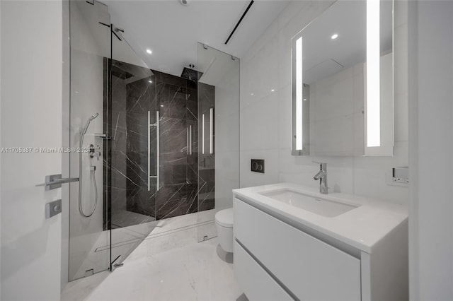 bathroom with a tile shower, vanity, toilet, and tile walls