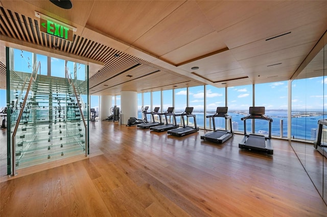 workout area featuring a water view, hardwood / wood-style floors, expansive windows, and wooden ceiling