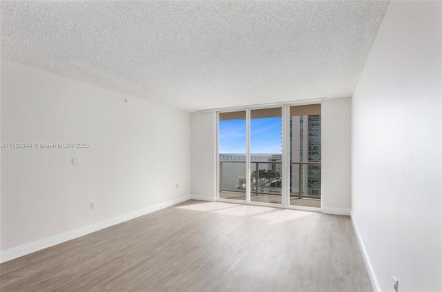 empty room featuring a textured ceiling, a wall of windows, and wood-type flooring