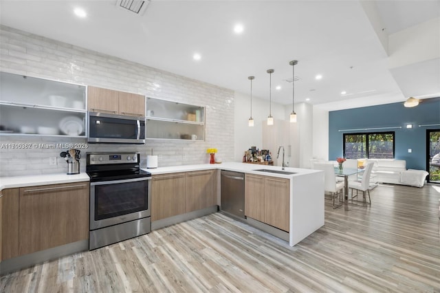 kitchen featuring light hardwood / wood-style floors, stainless steel appliances, decorative backsplash, hanging light fixtures, and sink