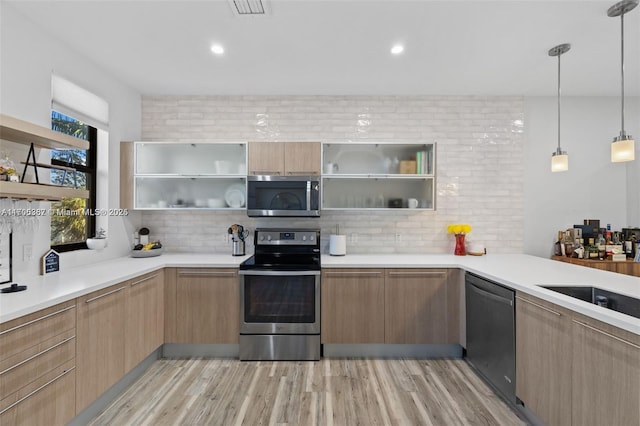 kitchen with appliances with stainless steel finishes, decorative light fixtures, decorative backsplash, kitchen peninsula, and light hardwood / wood-style flooring