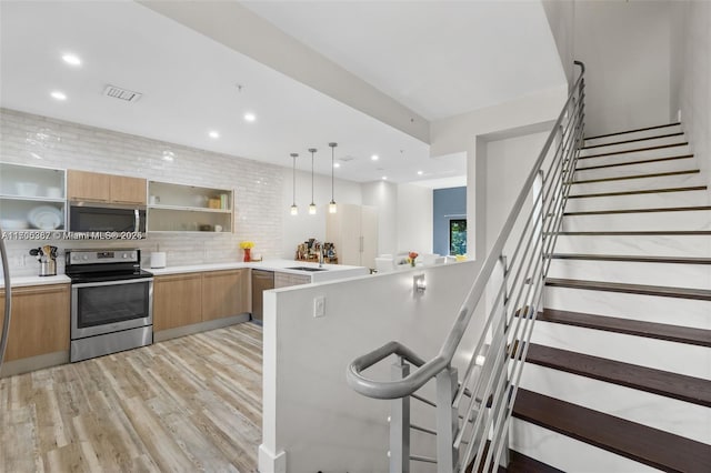 kitchen featuring pendant lighting, appliances with stainless steel finishes, tasteful backsplash, sink, and light wood-type flooring