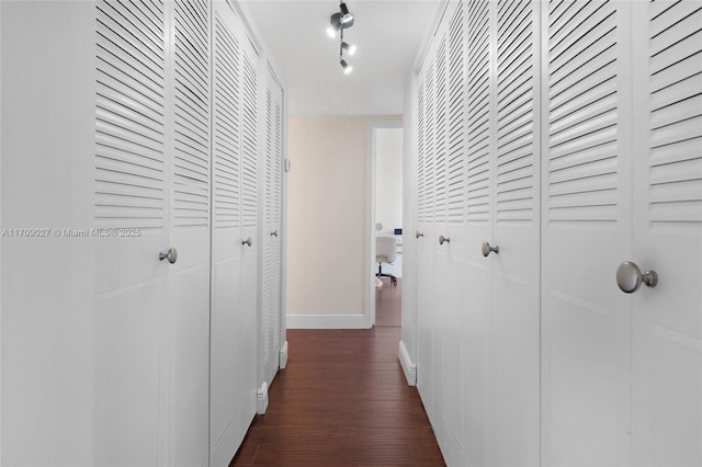 hallway with dark wood-style floors, rail lighting, and baseboards