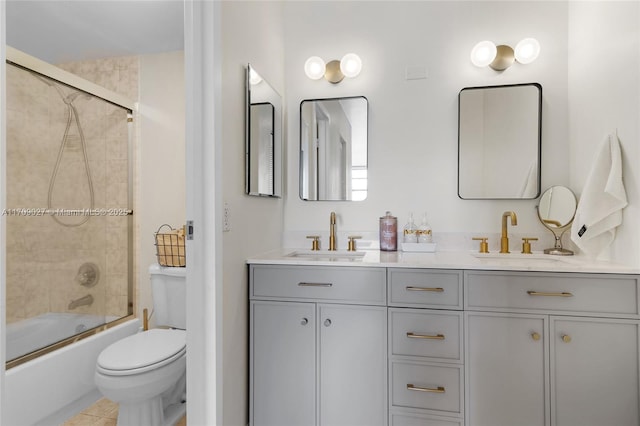 bathroom featuring toilet, double vanity, combined bath / shower with glass door, and a sink