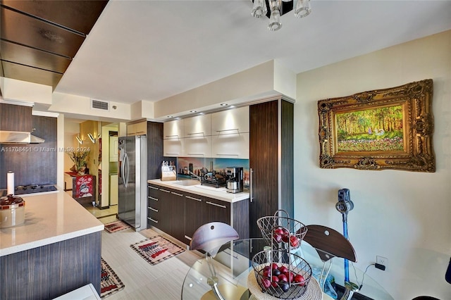 kitchen with dark brown cabinetry, extractor fan, sink, black gas cooktop, and stainless steel refrigerator