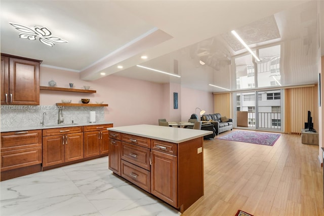 kitchen with decorative backsplash, ornamental molding, sink, light hardwood / wood-style flooring, and a center island