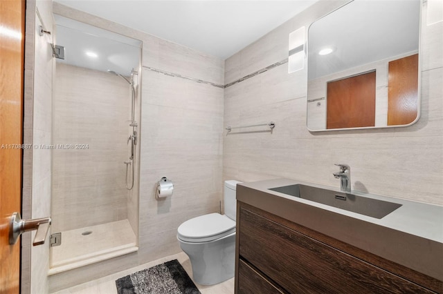 bathroom with a tile shower, vanity, tile walls, and toilet