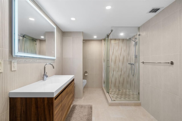 bathroom with tile patterned floors, vanity, tile walls, toilet, and a shower with shower door