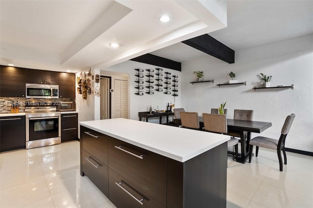 kitchen featuring appliances with stainless steel finishes, backsplash, dark brown cabinetry, a center island, and light tile patterned flooring