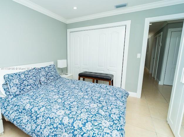 tiled bedroom featuring crown molding and a closet