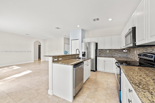 kitchen with appliances with stainless steel finishes, an island with sink, stone counters, white cabinets, and backsplash