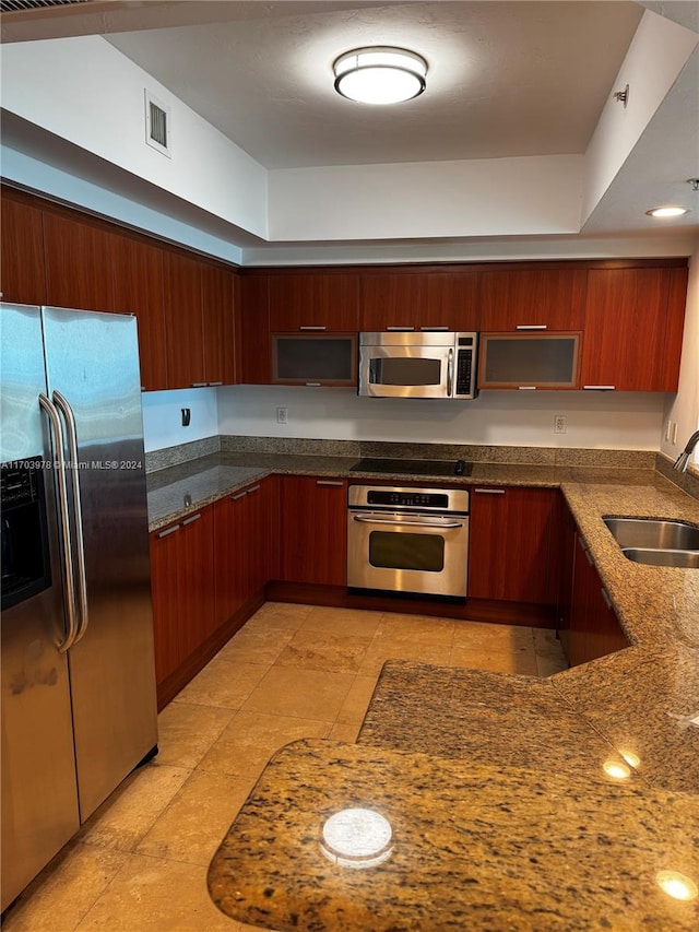 kitchen with a tray ceiling, sink, dark stone counters, and appliances with stainless steel finishes