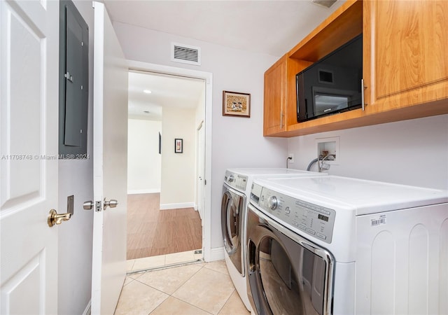 laundry room featuring washing machine and dryer, light tile patterned floors, and cabinets