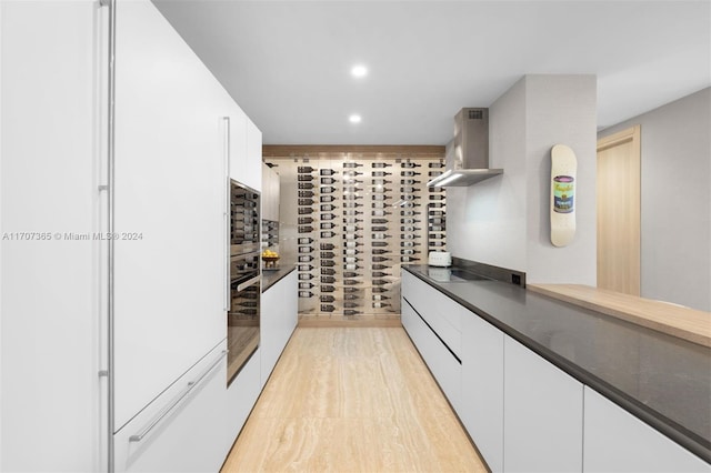 kitchen with decorative backsplash, wall chimney range hood, light hardwood / wood-style flooring, white cabinets, and oven