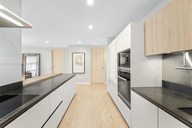 kitchen with light brown cabinetry, stainless steel appliances, white cabinetry, and light hardwood / wood-style floors