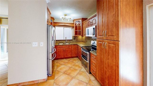 kitchen featuring backsplash, dark stone counters, a textured ceiling, appliances with stainless steel finishes, and light tile patterned flooring