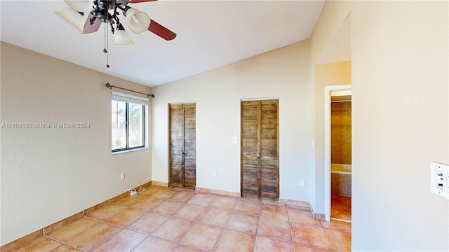 unfurnished bedroom with light tile patterned floors, two closets, ceiling fan, and lofted ceiling