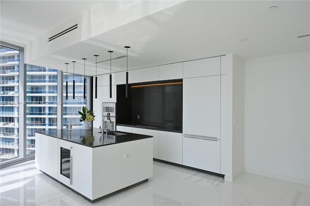 kitchen featuring white cabinetry, pendant lighting, floor to ceiling windows, and a kitchen island with sink