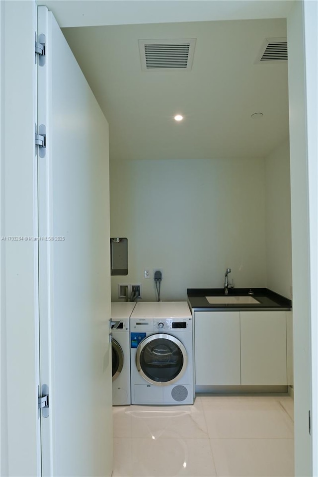 clothes washing area with cabinets, light tile patterned floors, washing machine and clothes dryer, and sink