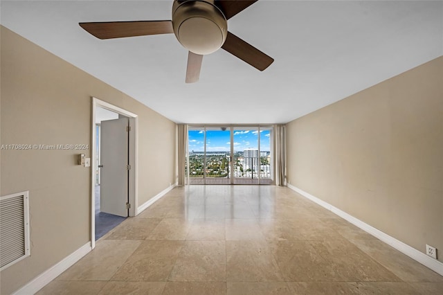 unfurnished room with ceiling fan and a wall of windows