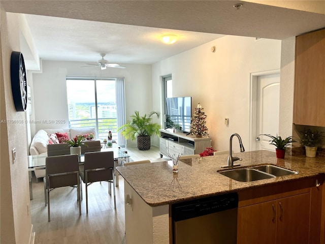 kitchen featuring a peninsula, stainless steel dishwasher, a sink, light wood-style floors, and light stone counters
