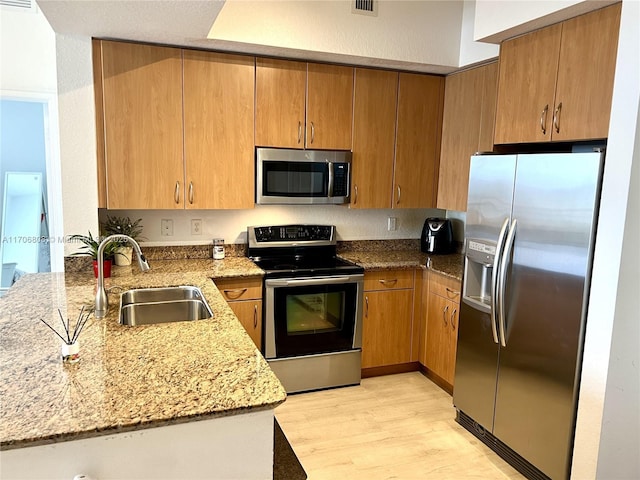 kitchen featuring a sink, light wood-style floors, a peninsula, appliances with stainless steel finishes, and light stone countertops