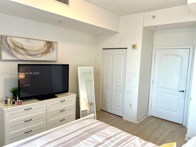 bedroom with light wood-type flooring, a closet, baseboards, and visible vents