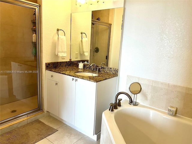 full bath with a bath, tile patterned flooring, a shower stall, a textured wall, and vanity