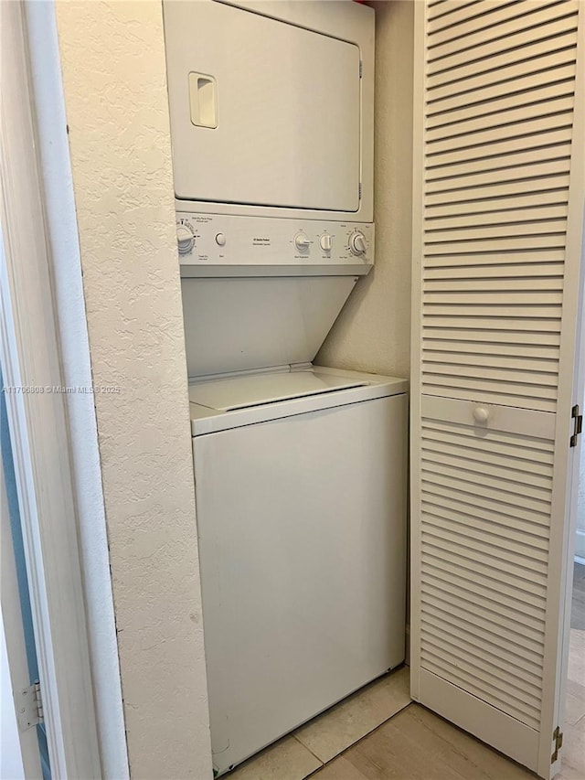 washroom featuring a textured wall, stacked washer / drying machine, and laundry area