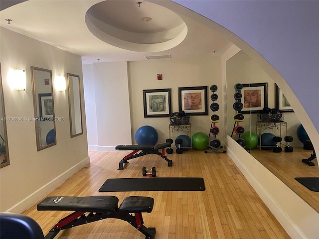 exercise room featuring hardwood / wood-style flooring, arched walkways, visible vents, and baseboards