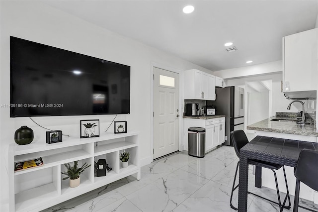 kitchen with white cabinets, light stone countertops, sink, and stainless steel refrigerator