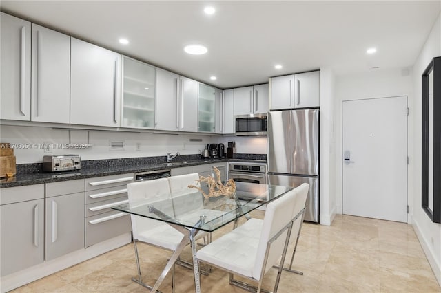 kitchen with stainless steel appliances, dark stone counters, and sink