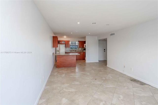 kitchen with white refrigerator with ice dispenser, backsplash, light stone countertops, light tile patterned flooring, and kitchen peninsula