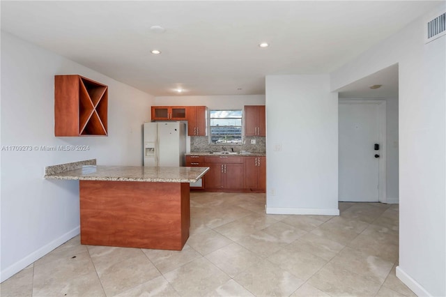 kitchen with kitchen peninsula, light stone countertops, backsplash, sink, and white fridge with ice dispenser