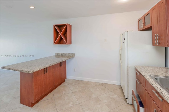 kitchen with kitchen peninsula, light stone counters, sink, light tile patterned floors, and white fridge