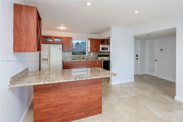 kitchen featuring kitchen peninsula, tasteful backsplash, light stone counters, white appliances, and light tile patterned flooring