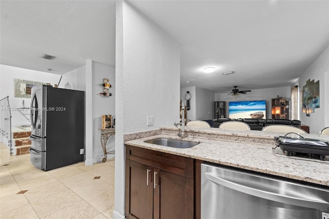 kitchen featuring ceiling fan, sink, light stone counters, dark brown cabinets, and appliances with stainless steel finishes