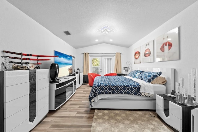 bedroom featuring a textured ceiling, french doors, light hardwood / wood-style flooring, and vaulted ceiling