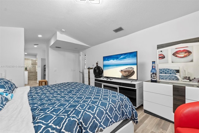 bedroom featuring a textured ceiling, light hardwood / wood-style floors, and lofted ceiling