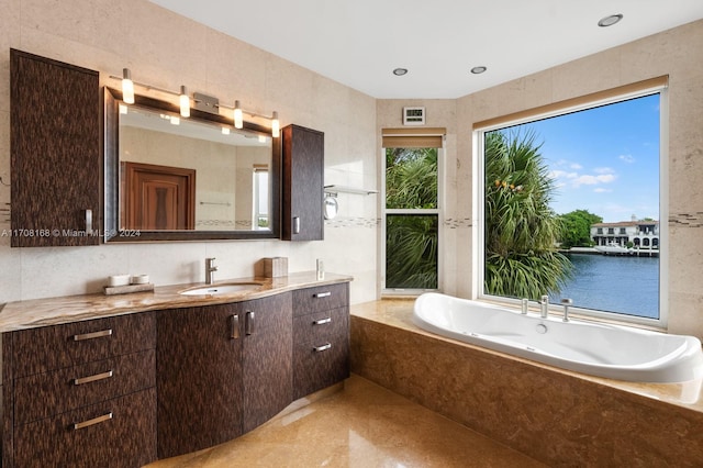 bathroom featuring tiled tub, vanity, a water view, and tile walls