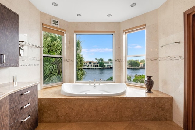 bathroom with tiled bath, vanity, a water view, and a healthy amount of sunlight