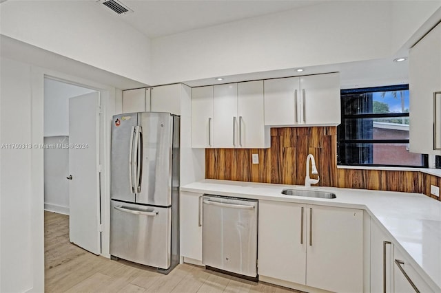 kitchen with appliances with stainless steel finishes, light hardwood / wood-style flooring, white cabinetry, and sink