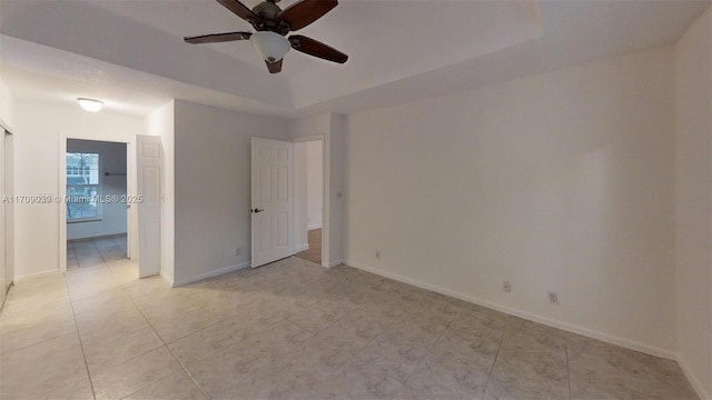 unfurnished bedroom featuring light tile patterned floors, ceiling fan, baseboards, and a raised ceiling