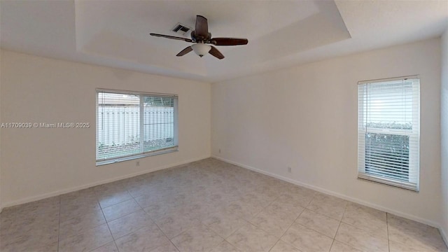 unfurnished room with a ceiling fan, a tray ceiling, visible vents, and baseboards