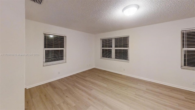 spare room with light wood-type flooring, visible vents, baseboards, and a textured ceiling