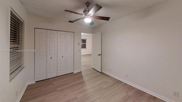 unfurnished bedroom with a closet, light wood-style floors, ceiling fan, a textured ceiling, and baseboards