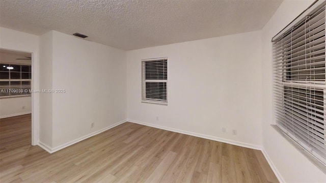 spare room with baseboards, a textured ceiling, visible vents, and light wood-style floors