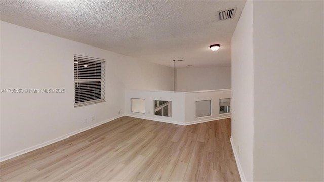 spare room with light wood-style floors, visible vents, a textured ceiling, and baseboards